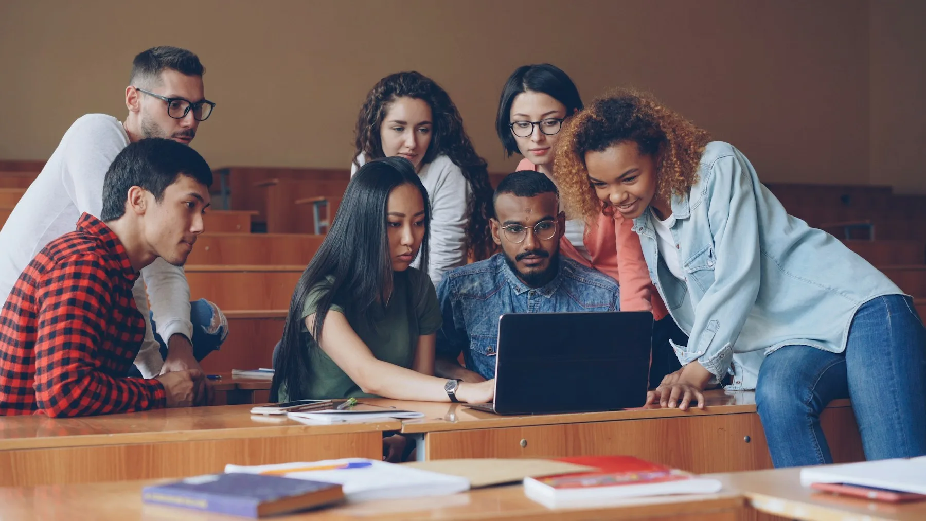 Students gathered around a laptop in a lecture hall