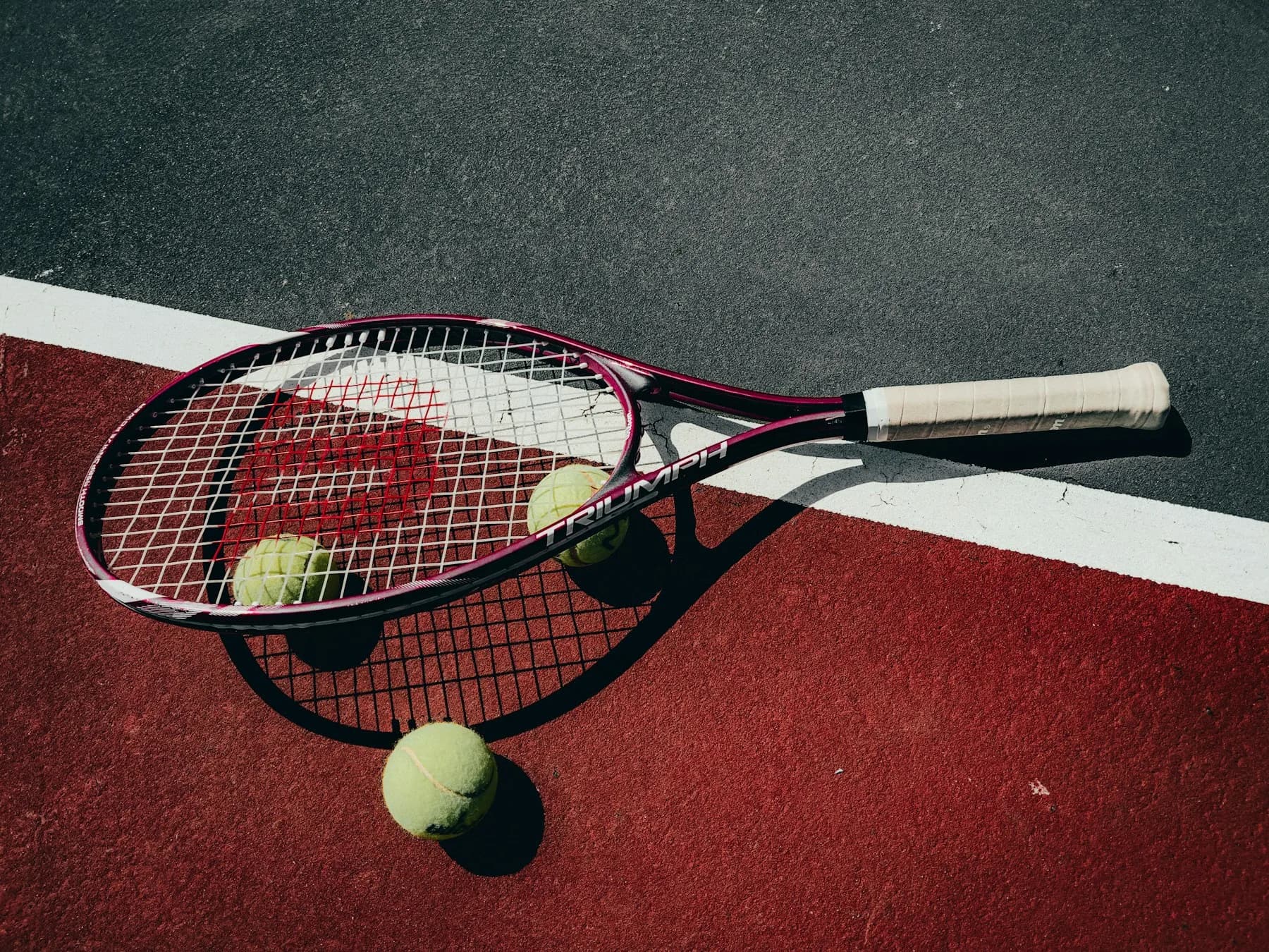 A tennis racket and balls on a red hard court